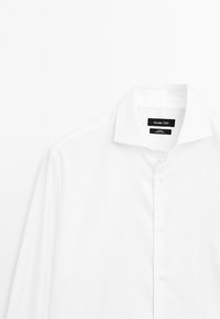 Hvid skjorte med lange ærmer med spredt krave og sort label med teksten Massimo Dutti, vist mod en ensfarvet hvid baggrund.