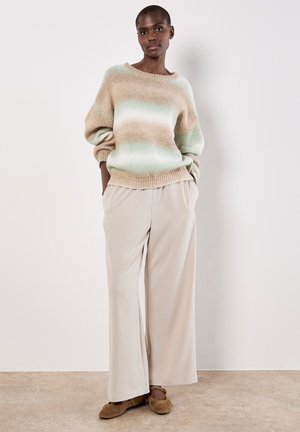 Pull en tricot beige doux avec un dégradé vert, manches larges et ourlet côtelé, assorti à un pantalon large beige clair et des ballerines marron.