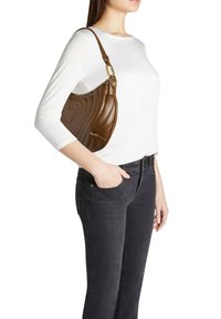 Borsa a tracolla in pelle marrone con forma curva, texture trapuntata con motivi a cuore e dettagli in oro, indossata sulla spalla.