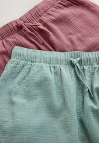 Deux paires de shorts en coton texturé, l'une bleu poussiéreux et l'autre rose pâle, toutes deux dotées de ceintures élastiques et de cordons de serrage.