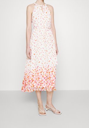 Frau trägt ein ärmelloses weißes Midikleid mit orange-rosa Blumenmuster und weiße, niedrigabsätzige Riemchensandalen.