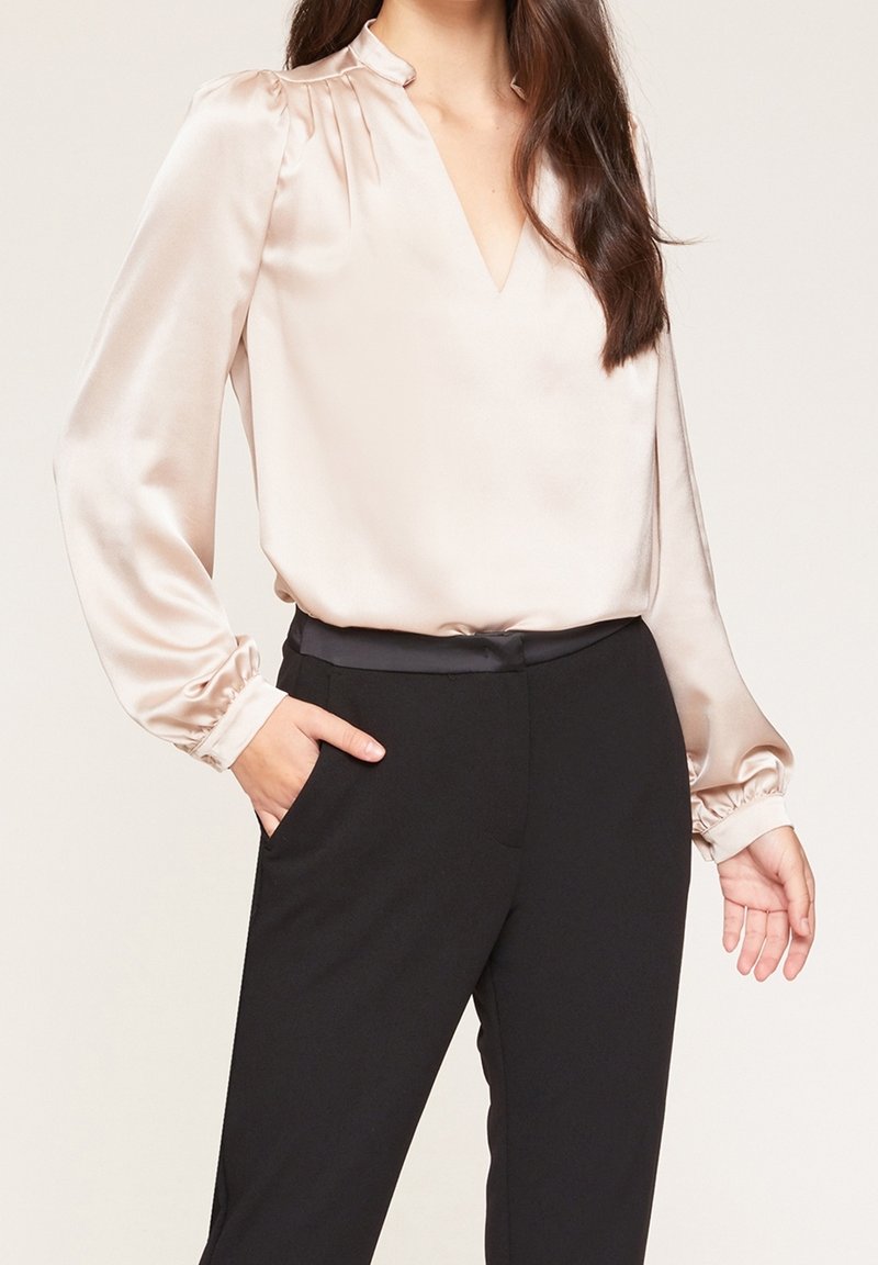 Satinblus i mjuk beige med V-ringning och samlade puffärmar, i kombination med svarta skräddarsydda byxor med sidofickor.