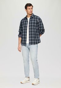 Marine geruite blouse met witte lijnen, lange mouwen opgerold bij de manchetten. Gecombineerd met lichtblauwe spijkerbroek en beige sneakers. Effen wit T-shirt eronder.