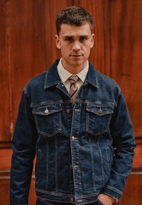 Jeans jakna v temno modri barvi s sprednjim gumbom, dvema prsnikoma in kontrastnim šivom; nosi se čez belo srajco s kragnico in kravato.