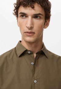 Camisa de botones verde oliva hecha de algodón suave, con cuello puntiagudo y botones grises. Diseño ajustado con textura mínima.