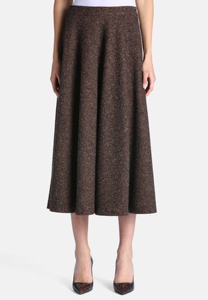 Femme portant une jupe marron évasée jusqu'aux genoux avec un motif texturé subtil et des talons hauts sombres à bouts pointus.