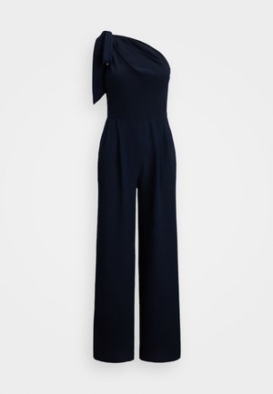 Marineblauwe jumpsuit met een enkel-schouderontwerp, voorzien van een geknoopte schouderband, wijdvallende broekspijpen en gestructureerde stof.