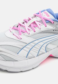 Bílé sportovní boty s vrchní částí z prodyšné a syntetické tkaniny, růžovými tkaničkami, modrými akcenty a texturovanou podrážkou s růžovými detaily.