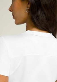 T-shirt bianco a maniche corte con scollatura rotonda, tessuto liscio e un logo sottile in rilievo sulla parte posteriore. Design semplice e minimalista.