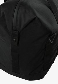 Bolsa de deporte negra con tejido texturizado, forma redondeada, correas en contraste y un zipper en la parte superior. Presenta hardware adicional en los laterales y detalle de botón.