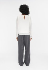 Blusa blanca de manga larga con un corte en forma de llave en la parte posterior, combinada con pantalones grises de corte holgado. Tejido suave, ajuste relajado.