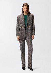 Dvostruki sako i odgovarajuće hlače od teksturirane smeđe tvida sa zlatnim dugmadi. Nositi preko zelene bluze i upariti s crnim štiklama.