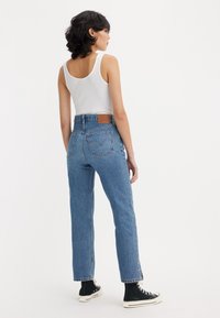 High-waisted blue denim jeans with a straight cut, featuring a classic five-pocket design, subtle fading, and a leather brand patch at the back.