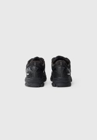 Schwarze Sport Schuhe aus Mesh und synthetischem Material, runde Form, strukturierte Akzente und gemusterte Belüftungsdetails an den Seiten.