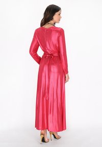 Abito lungo in satin rosa con maniche lunghe, cintura a fusciacca in vita e gonna fluente. Texture lucida e design elegante.