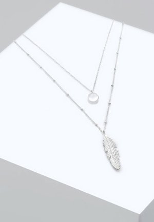 Collane argento a strati con un pendente circolare e un ciondolo a forma di foglia, entrambi su catene delicate con accenti di perline.