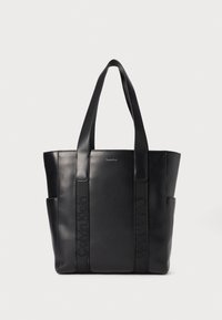 Sac en cuir noir avec double anses, présentant des détails de logo en relief et des poches latérales pour un espace de rangement supplémentaire. Fini lisse, design structuré.