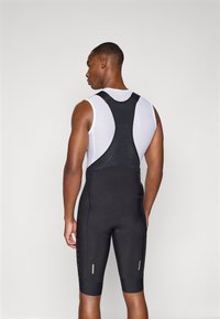 Schwarze Radsport-Bib-Shorts mit einem strukturierten weißen Oberteil, das ein Racerback-Design, reflektierende Akzente und ein gepolstertes Sitzpolster für Komfort aufweist.