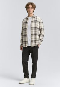 Lichtgekleurde geruite button-up shirt van katoen, gedragen over een wit T-shirt, gecombineerd met donkere broeken en witte sneakers.