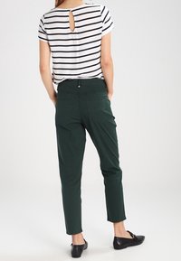 Haut à rayures à manches courtes avec un détail en clé à l'arrière ; associé à un pantalon tapered vert foncé. Les chaussures sont des ballerines noires.