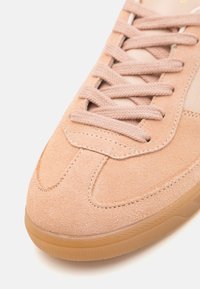 Baskets en daim rose pâle avec des lacets assortis et une semelle en gomme, montrant des coutures détaillées et la texture au niveau de la zone des orteils.