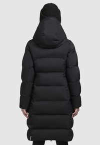 Zwarte pufferjas met een capuchon, voorzien van een doorgestikt ontwerp, lange lengte en elastische manchetten. Gladde textuur en minimalistische stijl.