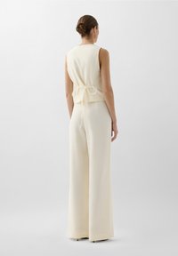Haut sans manches crème avec un nœud dans le dos, associé à un pantalon ample assorti, présentant un tissu texturé pour un look cohérent.