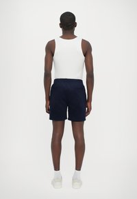 Shorts en velours côtelé bleu marine avec une taille élastique, deux poches arrière et une coupe décontractée, associés à un débardeur blanc et des baskets légères.