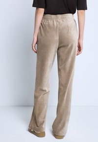Bežové manšestrové kalhoty s vertikálním žebrováním, pružným pasem a širokým střihem. Textilie má měkkou strukturu a hladký povrch.