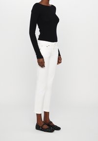 Svart långärmad topp med rund halsringning, ihopparad med vita slim-fit jeans och svarta ballerina skor med vita prickar.