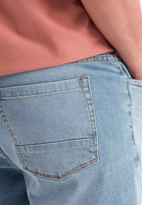 Ljusblå denimjeans med en bakficka, med orange sömmar. Tyget har en mjuk textur och en avslappnad passform.