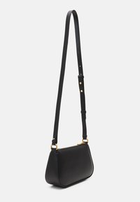 Sac à bandoulière en cuir noir avec une base arrondie, une sangle mince et des accents en métal doré. Surface texturée avec une fermeture éclair.