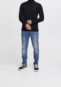 Pull à col roulé noir, jean bleu, baskets noires et blanches. Tenue décontractée au style ajusté avec une texture côtelée et un léger délavage sur le jean.