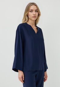Marineblaue, langärmelige Bluse mit V-Ausschnitt und lockerer Passform. Glatter Stoff, minimalistischem Design, mit einer Brustnaht als Detail.