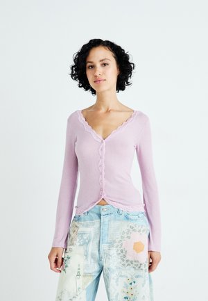 Lichtroze geribbelde langemouwen cardigan met een scalloped halslijn en knoopsluiting, gecombineerd met blauwe patchwork jeans met bloemmotieven.