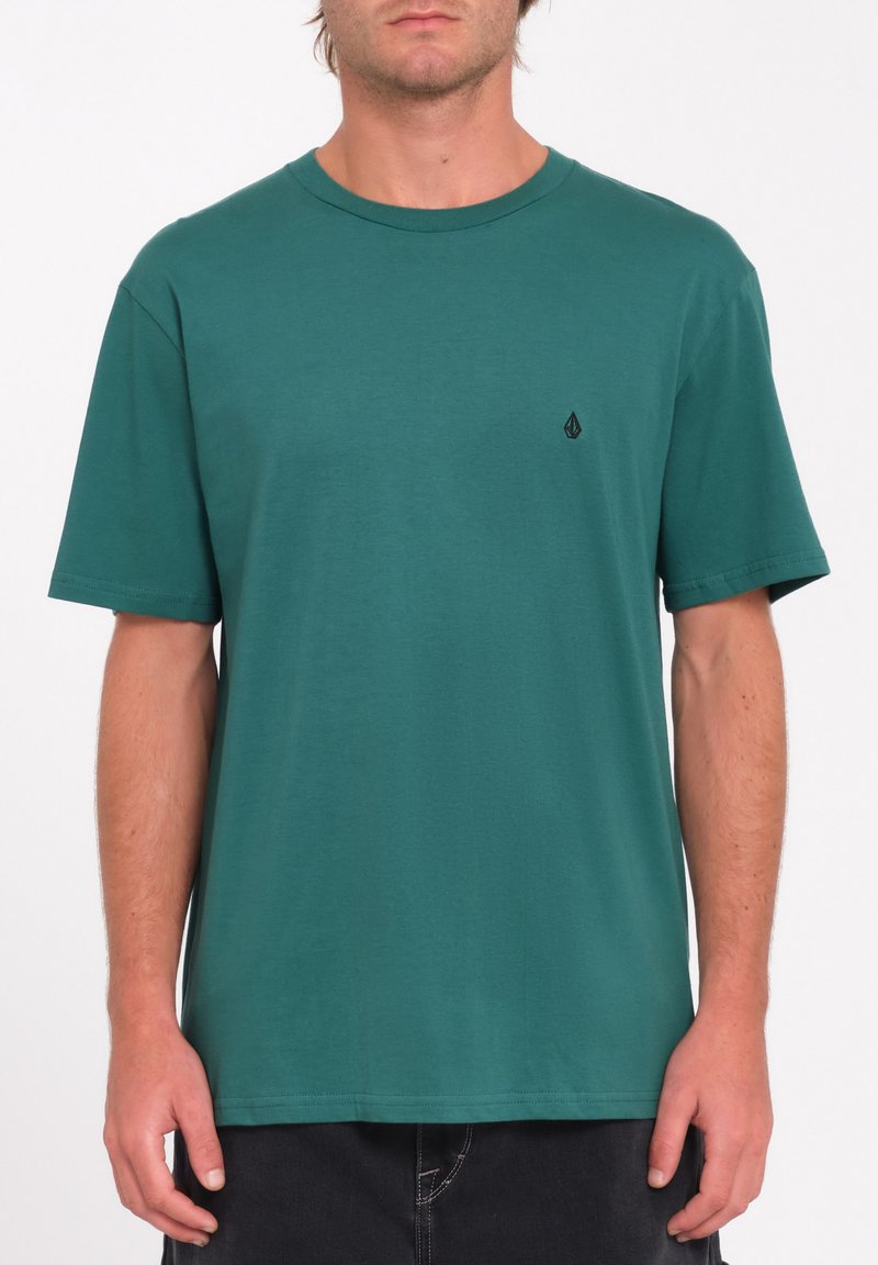T-shirt vert canard à manches courtes en coton, avec un col ras du cou et un petit logo noir sur la partie gauche de la poitrine.