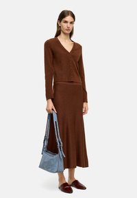 Brązowy sweter z dzianiny z dekoltem w serek i guzikami, dopasowana brązowa spódnica, niebieska torebka na ramię z paskami oraz bordowe buty na slip-on.