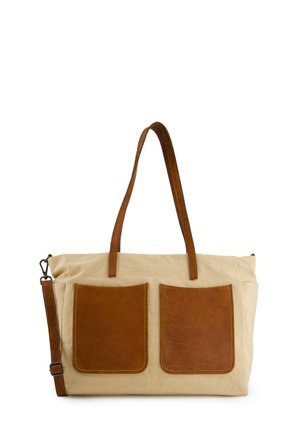 Beige canvas tote bag with two large brown leather front pockets, long leather shoulder strap, and two leather handles.