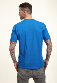 Camiseta de algodón azul con mangas cortas, corte estándar y neckline redondo. La tela parece suave, con costuras visibles y un diseño casual.