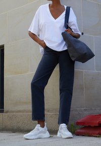 Camiseta blanca de cuello en V, jeans rectos de color azul oscuro y zapatillas de color claro. Llevando un bolso gris texturizado con forma curva.