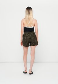 Black and white cross-back tank top paired with olive green shorts featuring a leopard print. The individual wears black heeled sandals.