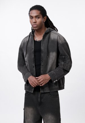 Jeansjacke in verblasstem Schwarz mit Kapuze, großen Taschen und Knopfakzenten. Kombiniert mit passenden, abgetragenen Jeans.