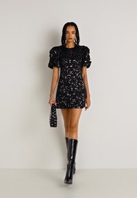 Crna mini haljina s napuhanim rukavima, cvjetnim uzorkom, teksturiranim materijalom. Uparena s crnim čizmama do koljena i torbicom s čavlima.