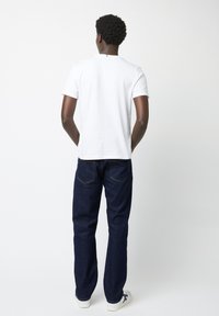 Witte katoenen t-shirt gecombineerd met donkerblauwe spijkerbroek. De spijkerbroek heeft een klassieke snit, met subtiele stiksels op de achterzakken.