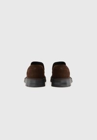 Chaussons en daim marron avec un bout arrondi et une semelle en caoutchouc noir. Présente des accents de couture et un logo sur le talon.