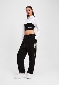 Black cropped sweatshirt with white collar and logo, paired with black sweatpants featuring white branding, complemented by white platform sneakers.