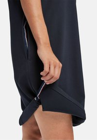 Rochie bleumarin dintr-un material texturat, cu o tiv curbat. Dispune de o buzunar lateral cu un tab de deschidere cu dungi.