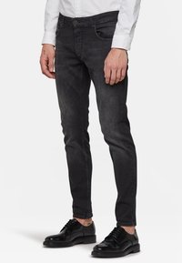 Mörkgrå smalpassande jeans för män med svag slitning, fem fickor och knappgylf, parat med blanka svarta kostymskor.