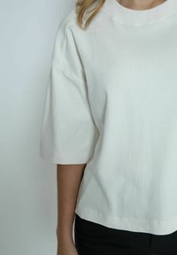 White cotton t-shirt with a relaxed fit, dropped shoulders, and short sleeves. Smooth texture with a crew neckline and a cropped hem.