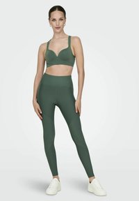 Green sports bra with a low V-neck design and thick straps, paired with high-waisted matching leggings featuring angular seam details.